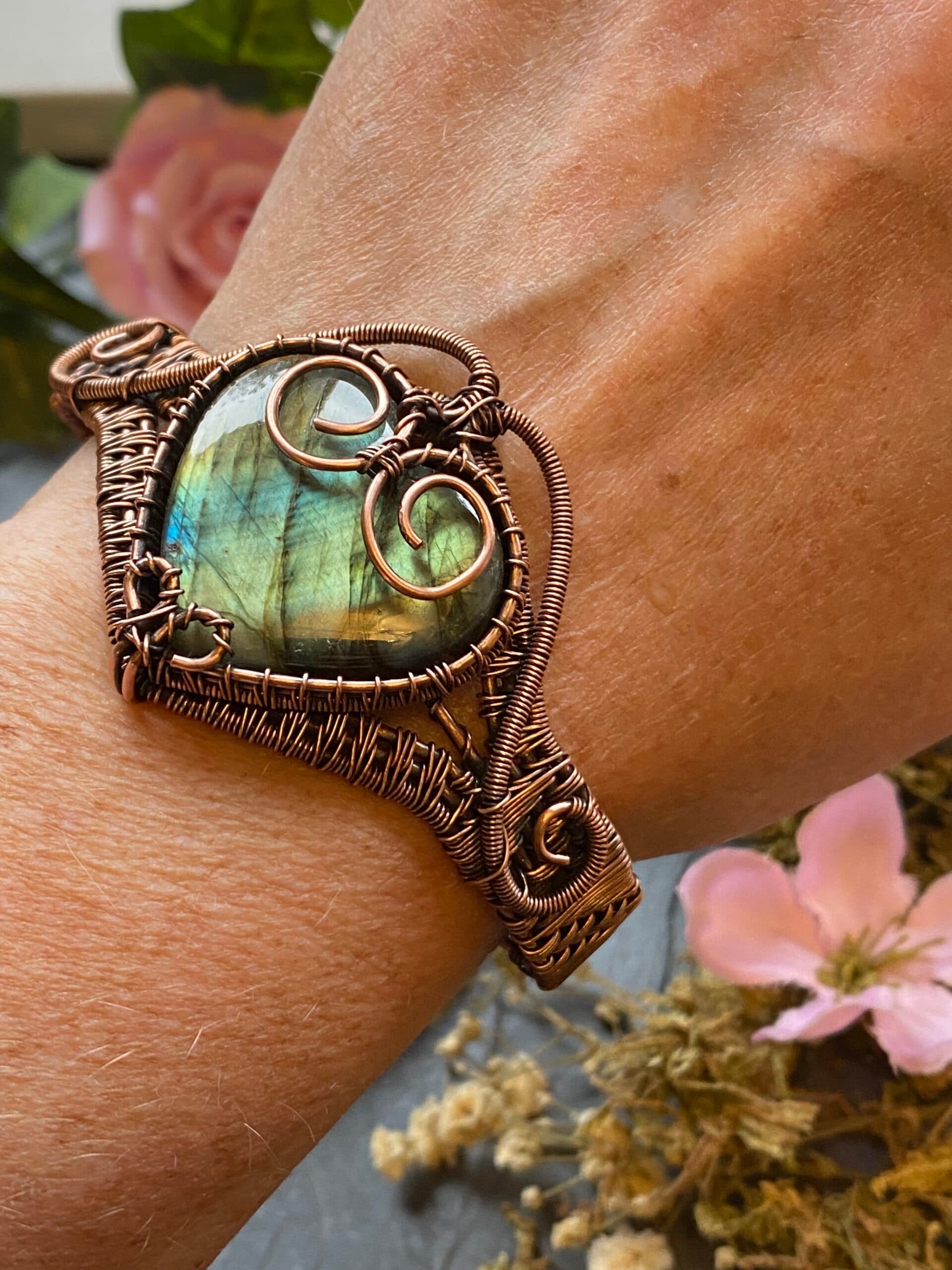 Close-up of heart-shaped labradorite cabochon with golden flash, framed by decorative copper curls and woven wire setting.