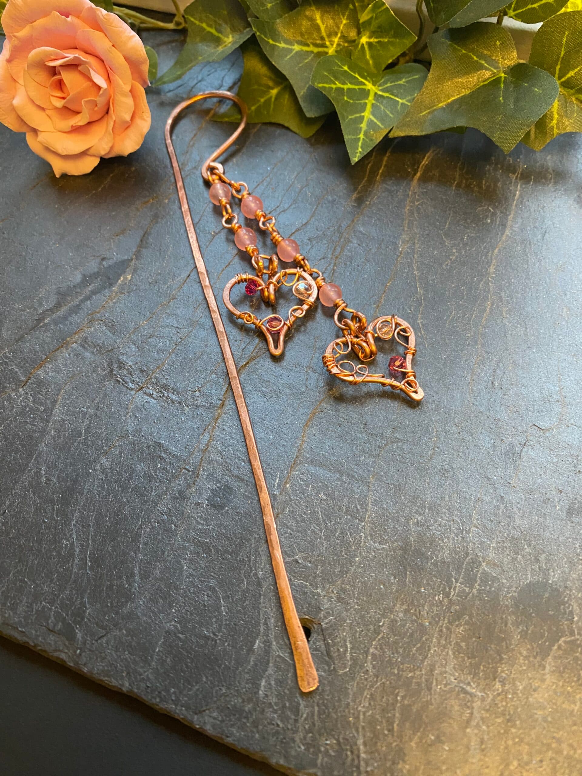 Handmade copper bookmark with two hearts and pink beads on shepherd’s crook chain over hardback book spine
