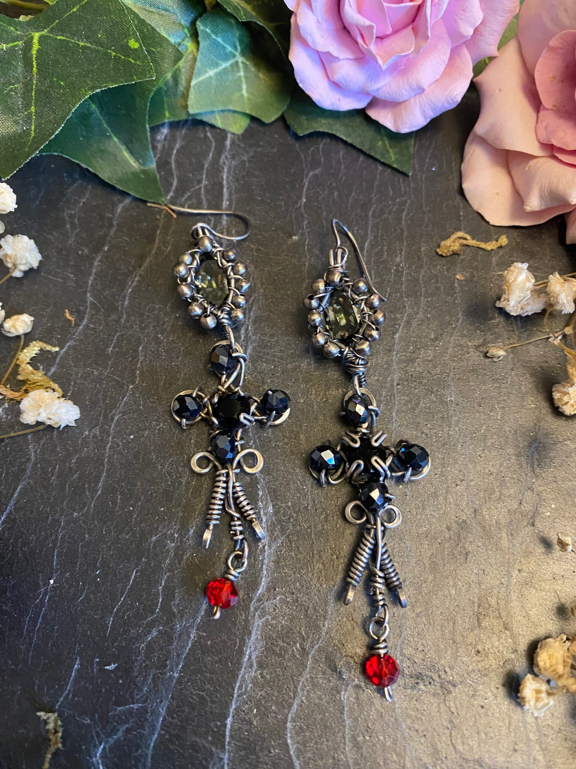 Pair of handmade gothic earrings featuring antiqued silver filled wire, black and grey Swarovski crystals, red and black beads and long decorative drops.