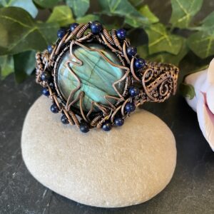 Handwoven copper wolf head cuff bracelet with labradorite and lapis lazuli beads Copper wolf head cuff showing woven wire detail and gemstone centerpiece Handwoven copper cuff bracelet with hammered wolf symbol and mystical stones