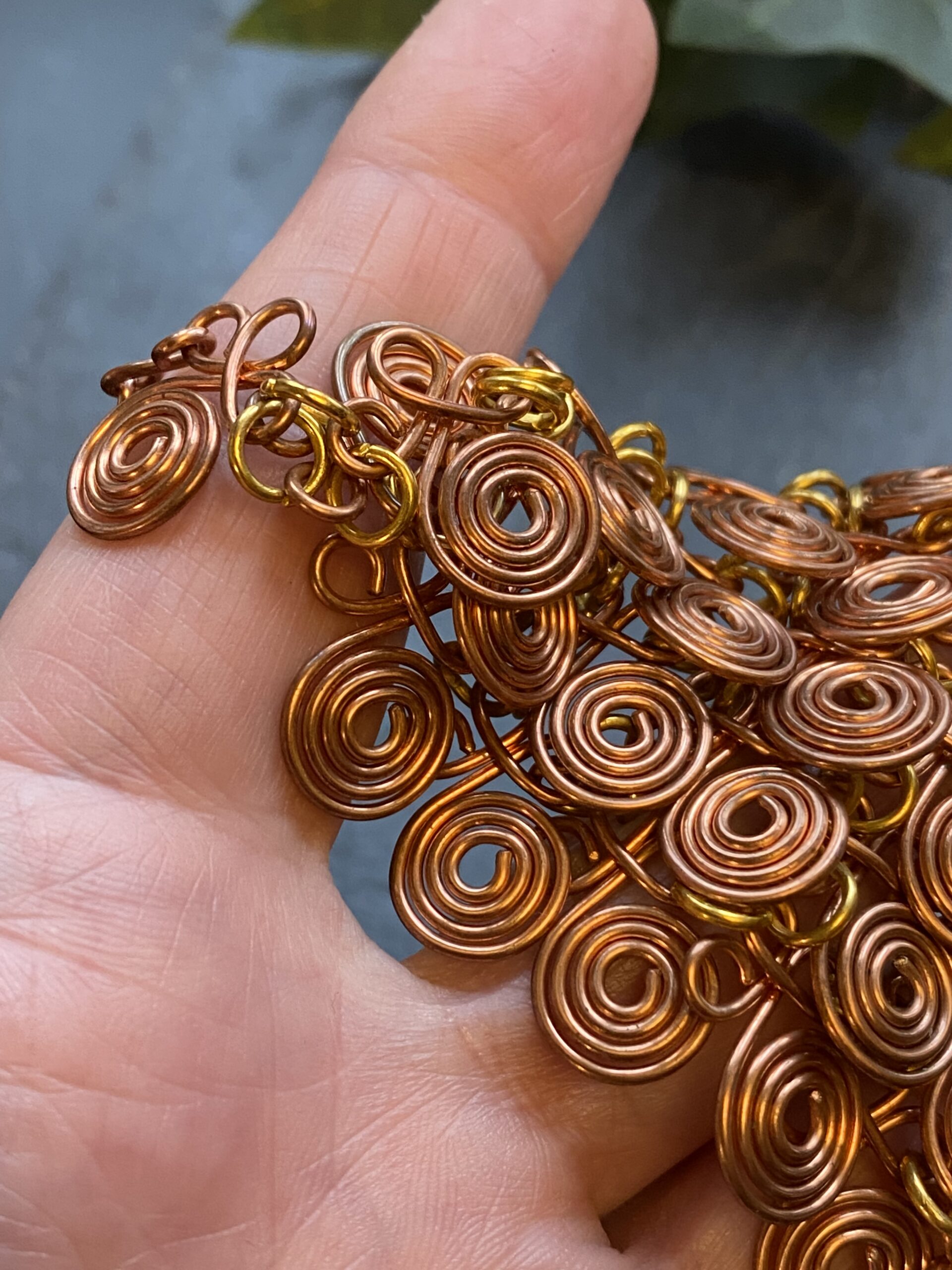 Copper chain mail necklace with spiral wire components and brass jump rings in a fluid V shape