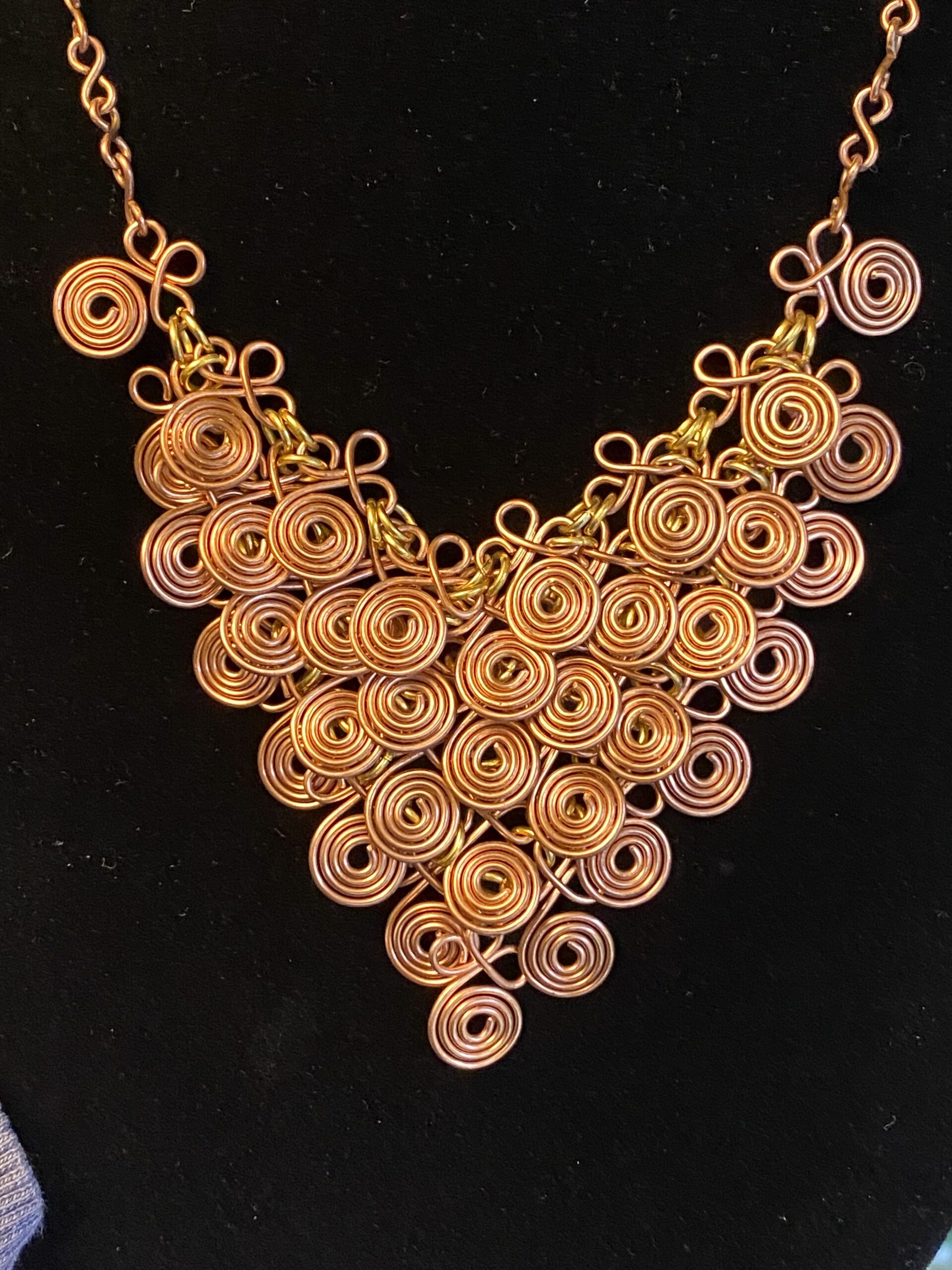 Copper chain mail necklace with spiral wire components and brass jump rings in a fluid V shape
